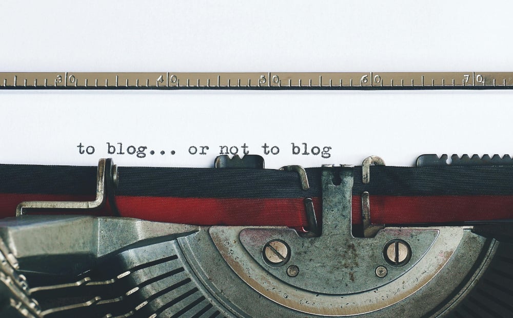 A typewriter typing the words 'to blog... or not to blog' on piece of paper.