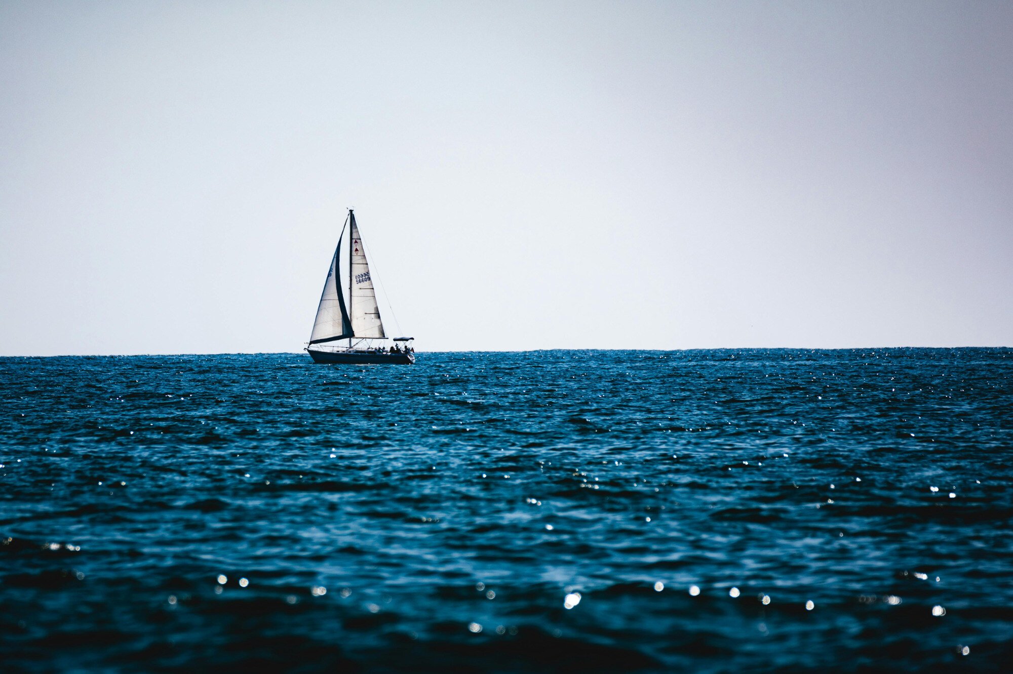 A small sale boat near the horizon in front of a body of water.