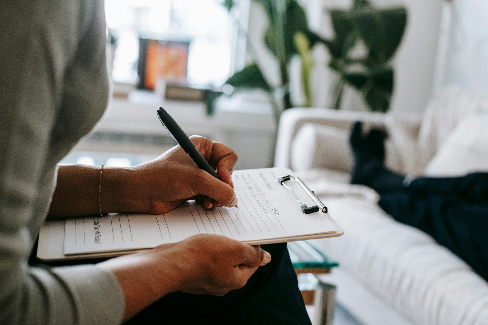 Person writing on clipboard in front of couch.