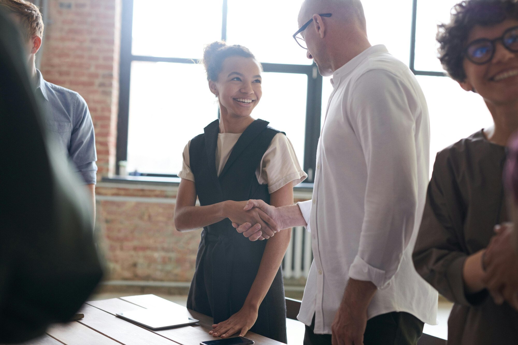 Two business people shaking hands over wooden table and smiling.