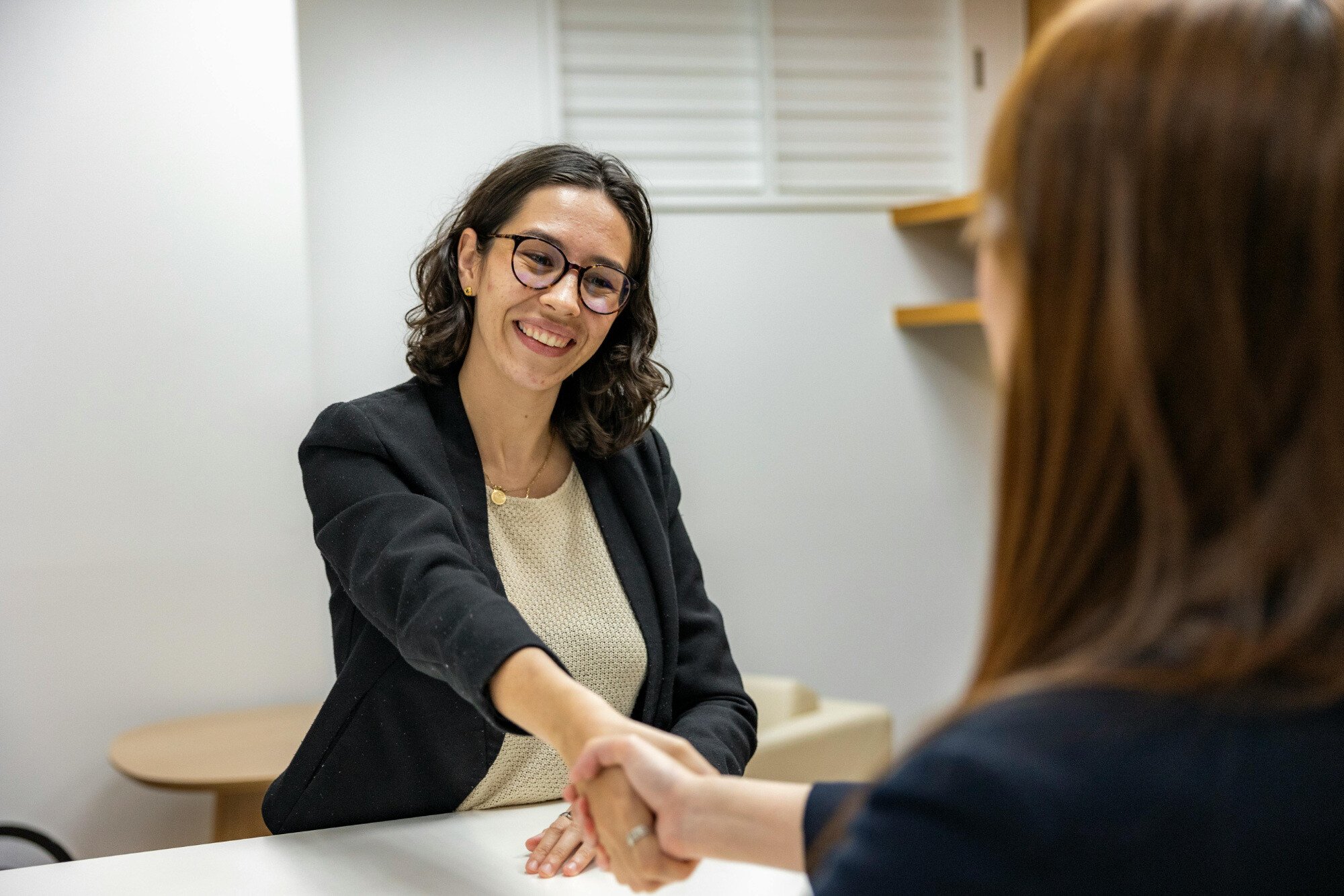 Two office workers shaking hands over desk.