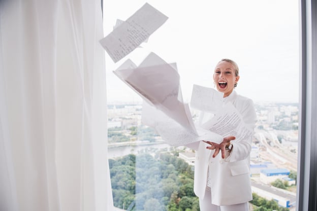 Business person standing at office window throwing documents in the air.