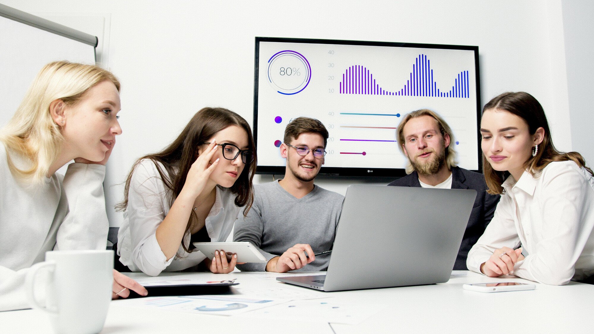 Five happy office workers looking at a laptop with a screen showing statistics graphs behind them.