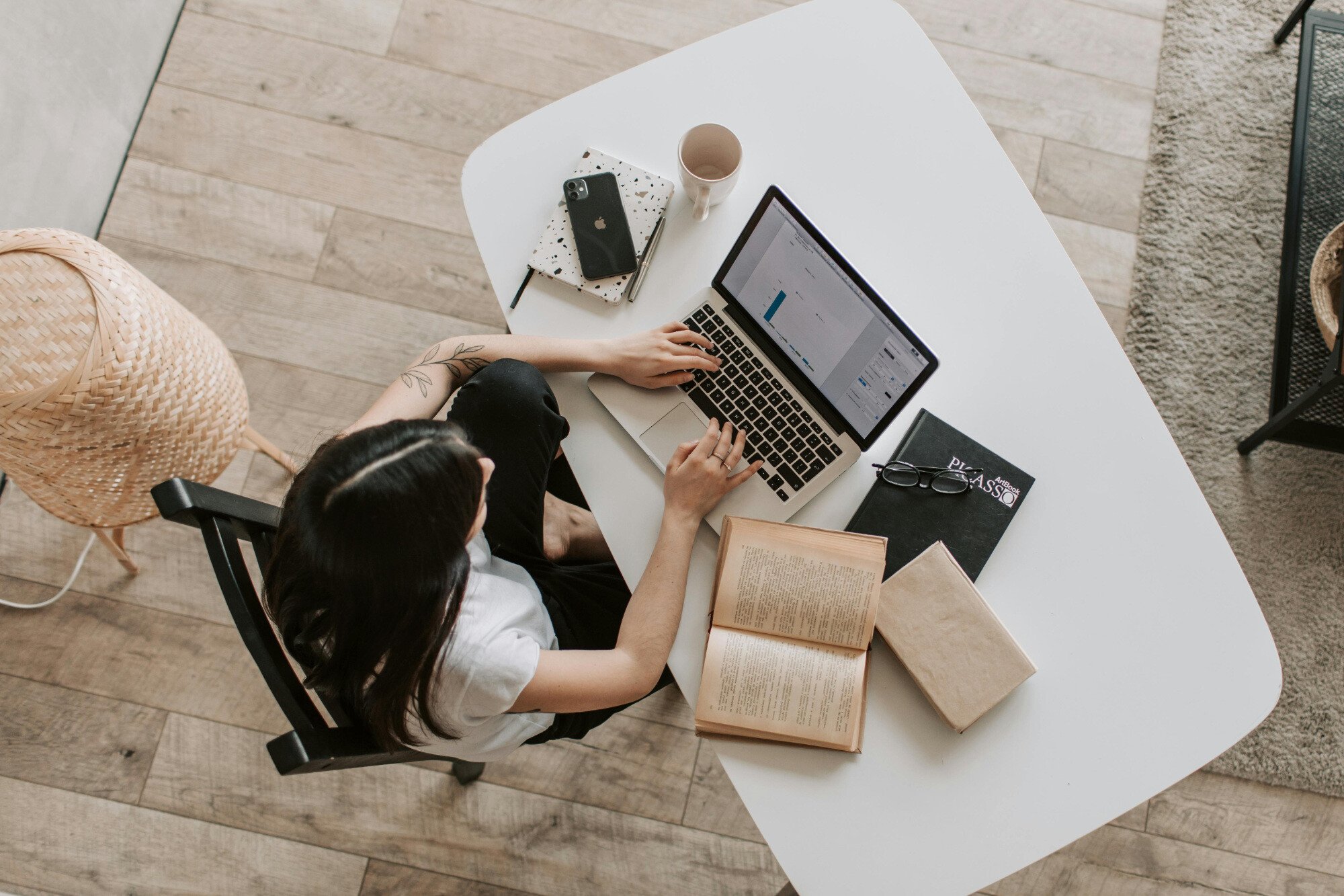 Person sitting at their desk at home typing on laptop surrounded by books and notebooks.