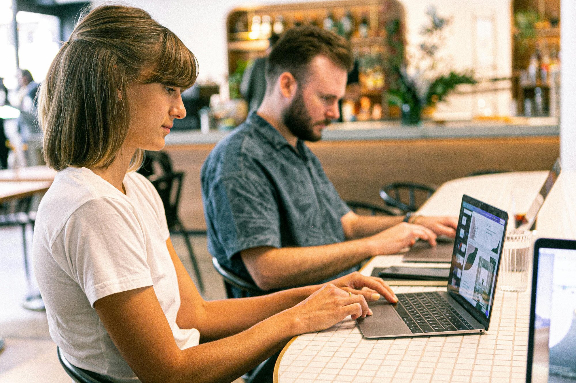 Two office workers sat at desk typing on laptops.