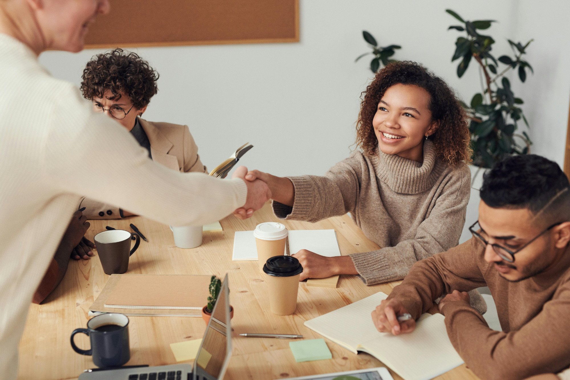 Four people sitting around office desk with the two in the middle shaking hands.