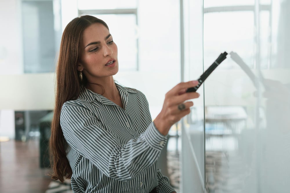 Office worker pointing pen at notes written on a whiteboard.