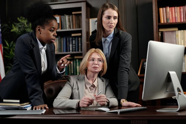 Three workers at office desk looking at desktop computer.