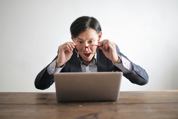 Man staring at laptop screen through his glasses with really surprised look on his face.