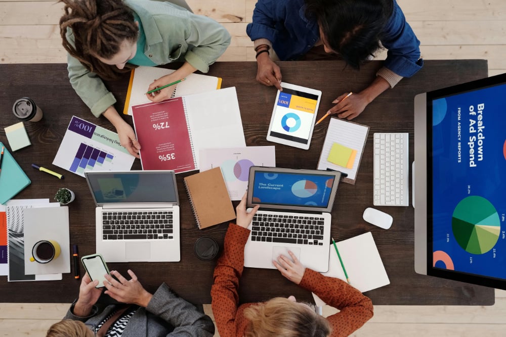 Overhead view of office workers sitting at desk with laptops and various business strategy charts.