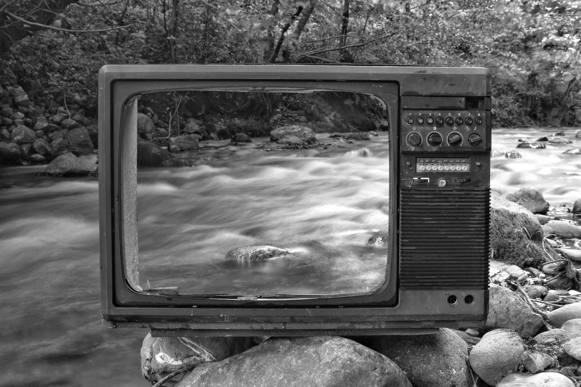 Front of an old television with screen carved out, sat in front of a river.