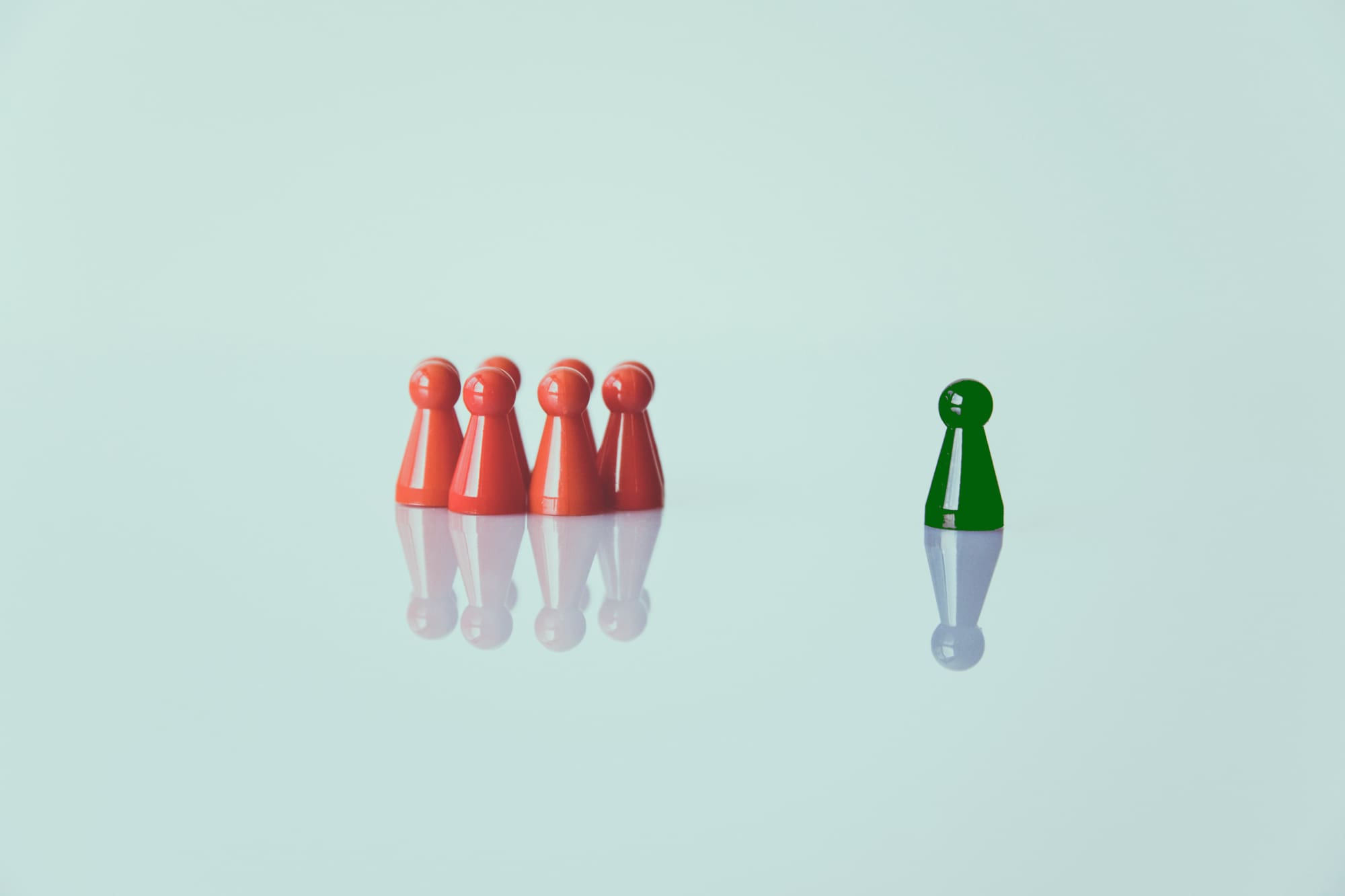 One green chess piece standing separate from a group of red ones.