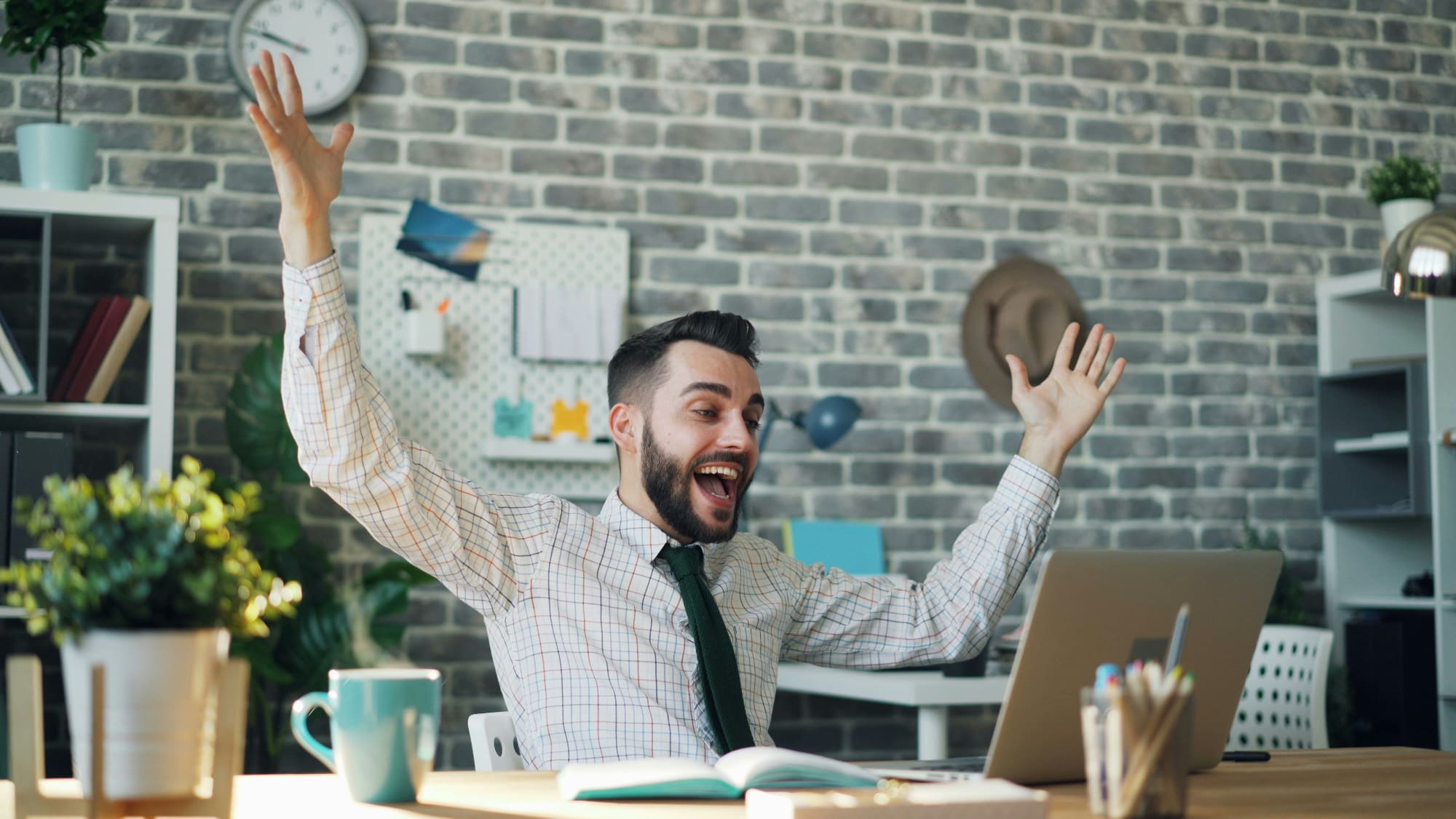 Office worker celebrating at desk with hands in the air.
