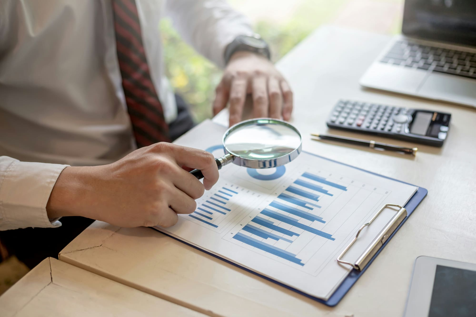 A business person sitting at desk using magnifying glass to look at business charts.