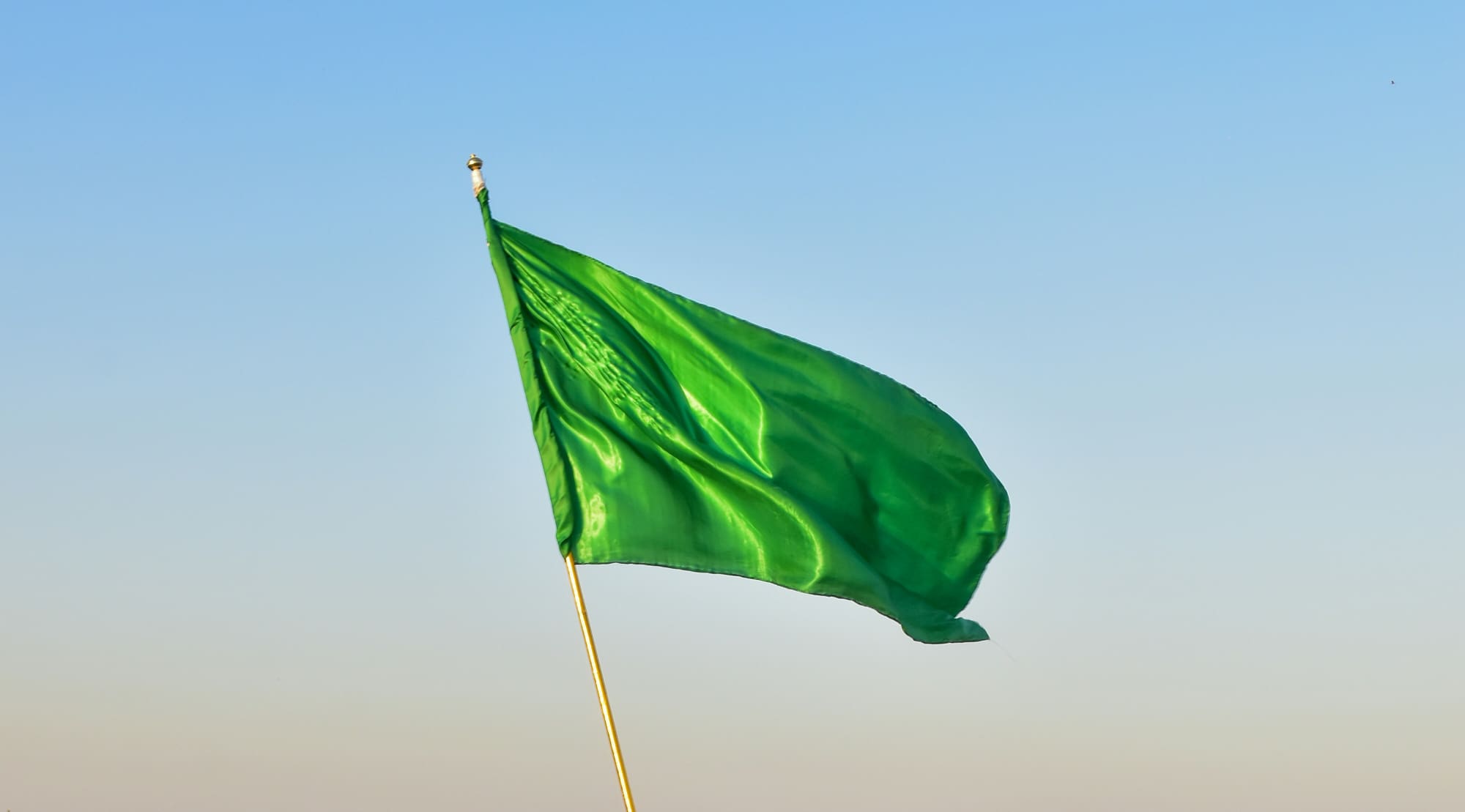 A green flag flying with sky blue background.
