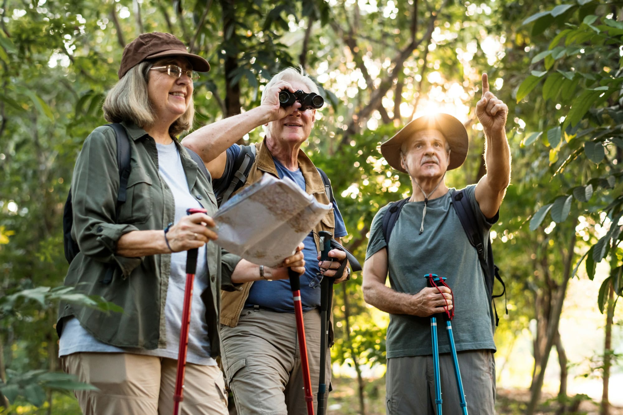 Three people in the jungle looking at a map and using binoculars to search for something.