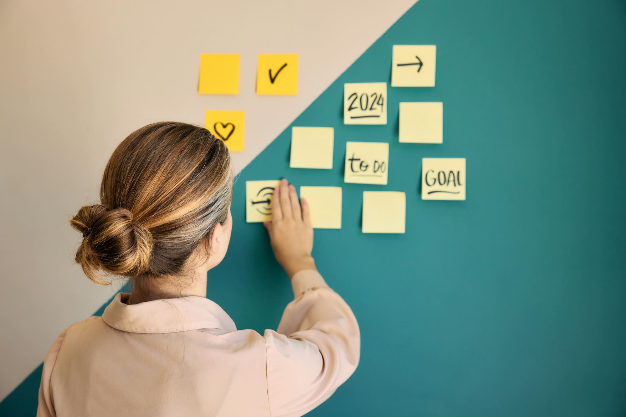 Woman putting goal-planning post-it notes on a green and cream wall.