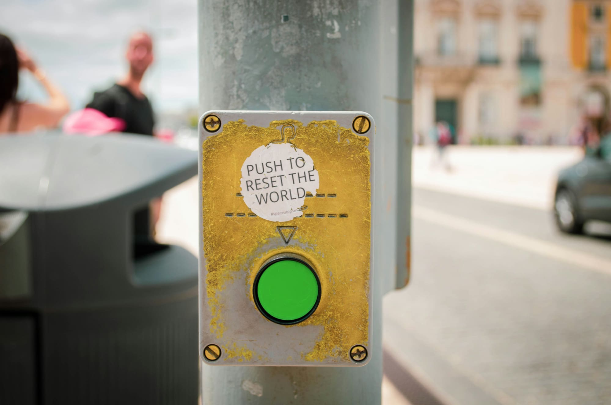 A green button attached to a street pole with the words 'Push to reset the world' written above it.