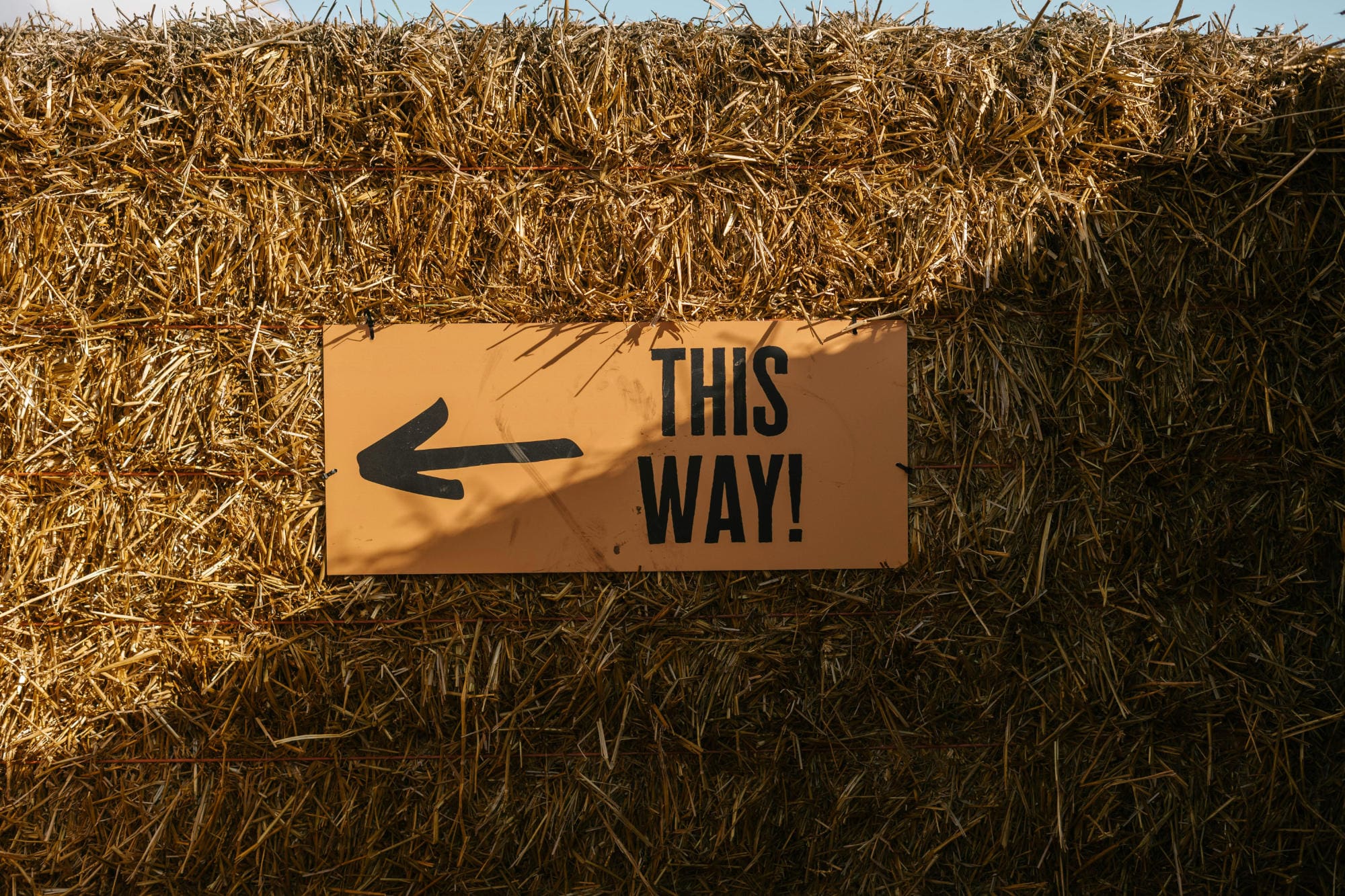 A sign saying 'this way' attached to a wall of hay.