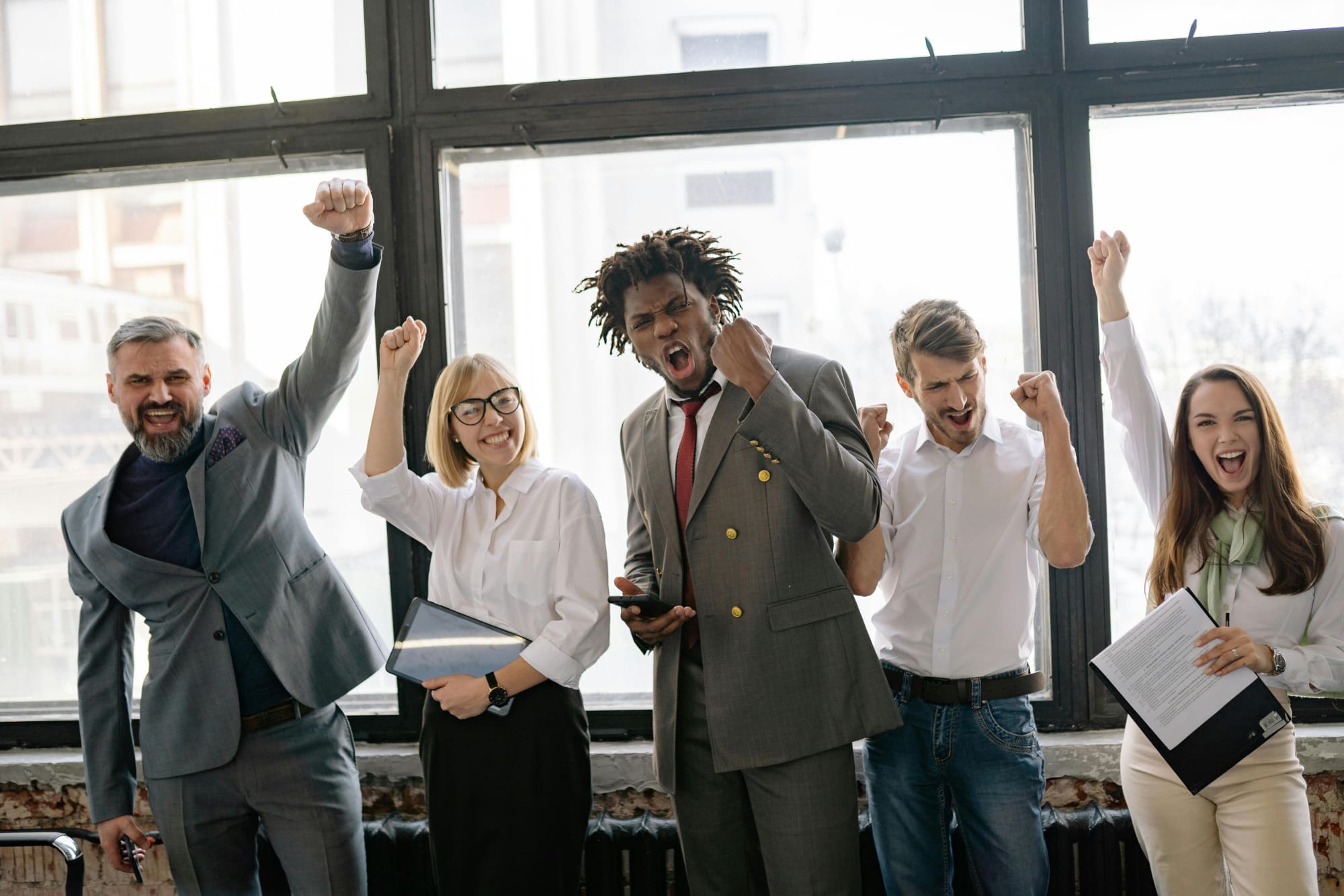 Five office workers holding clipboards and celebrating with hands in the air.