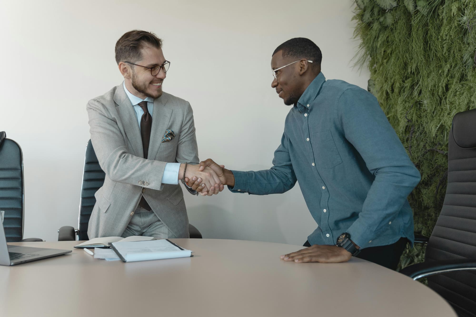 Two office workers shaking hands over a desk.