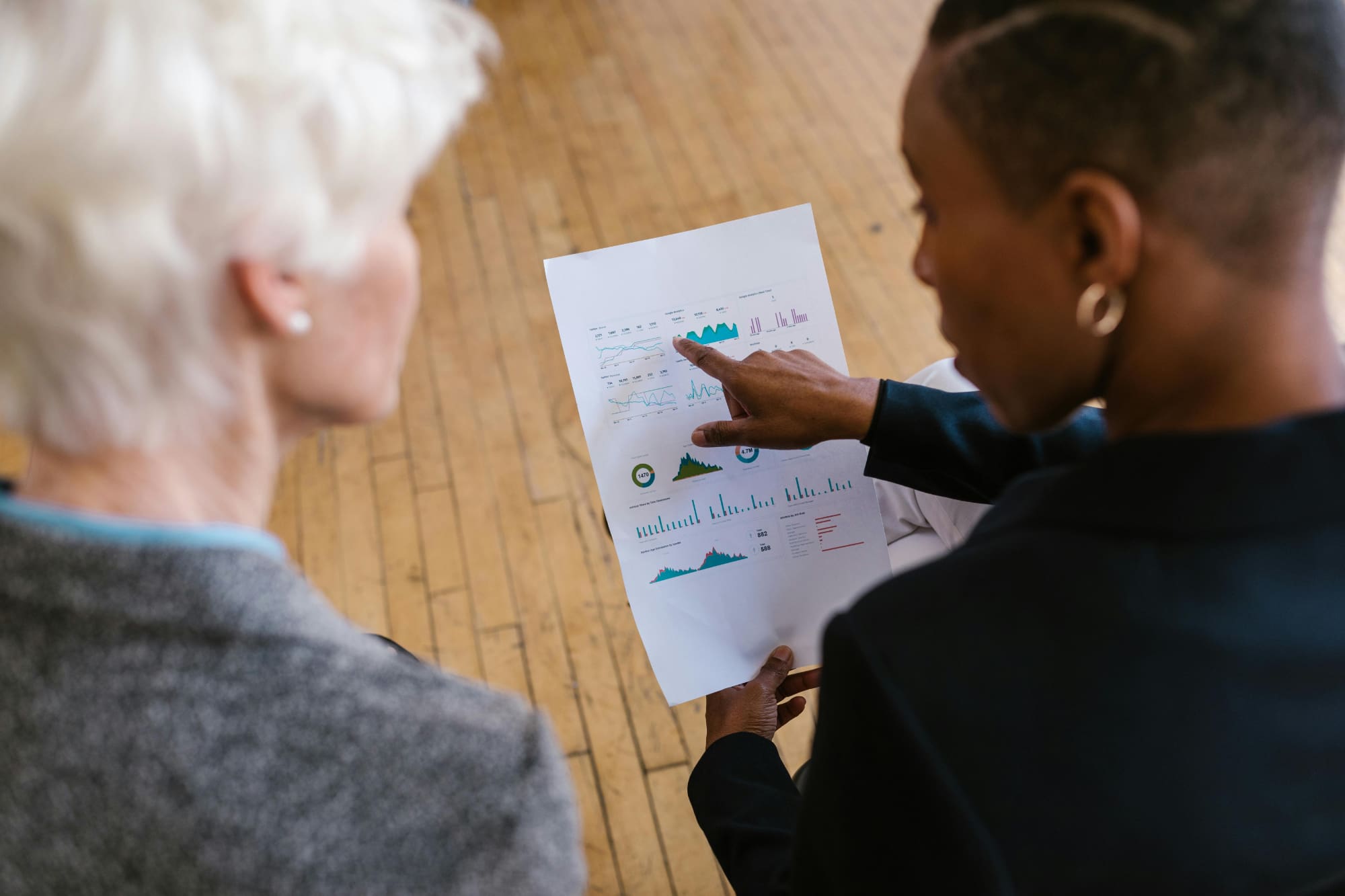 One office worker pointing at a page with statistics on it with another office worker beside them.