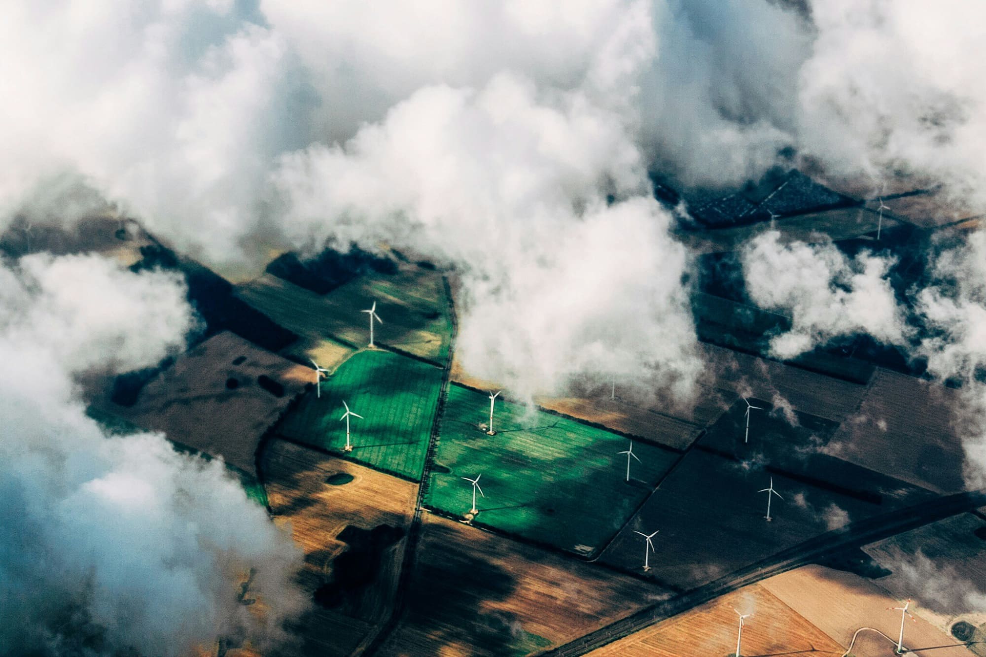 View from above clouds of green fields with wind turbines in them.