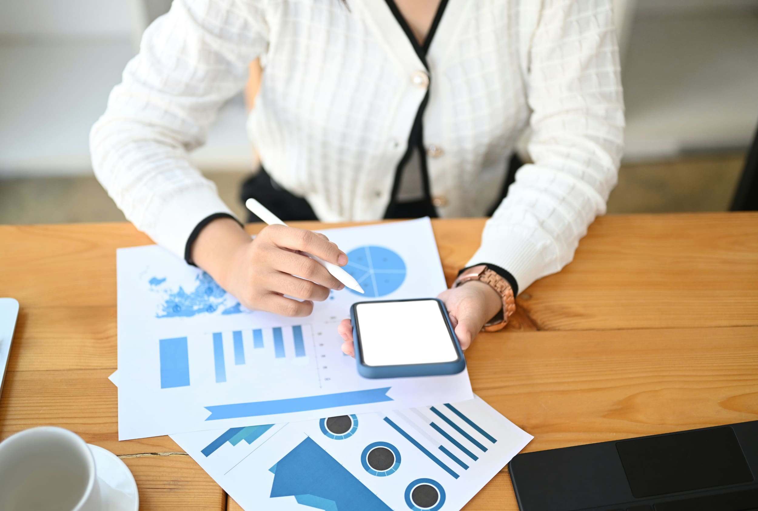 An office worker at a desk with business graphs in front of them working something out on a tablet.