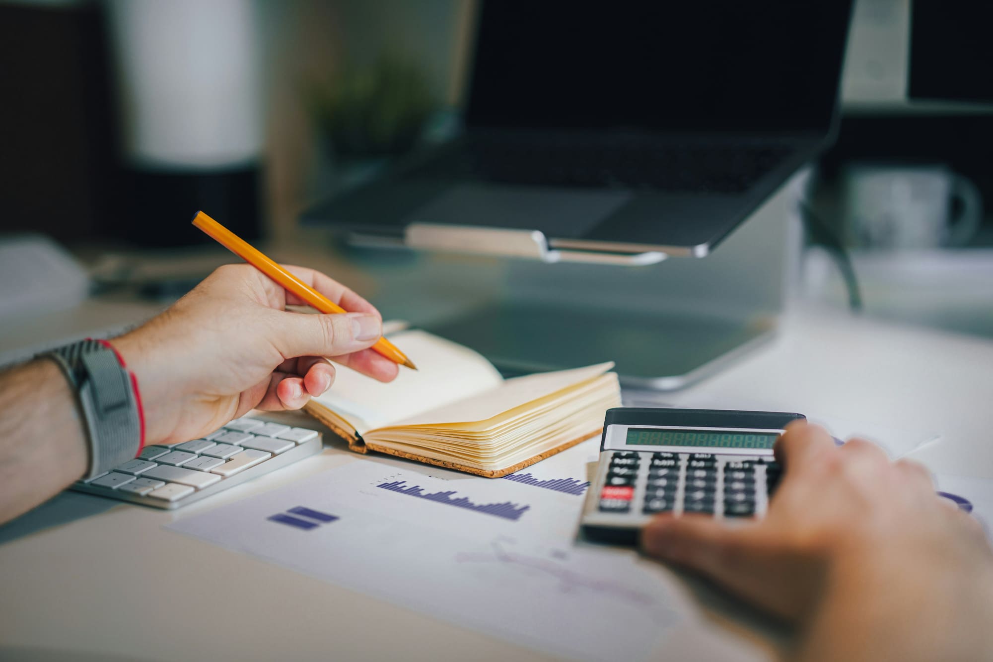 Somebody sitting at desk, with one hand working a calculator and the other writing down notes in a notebook.