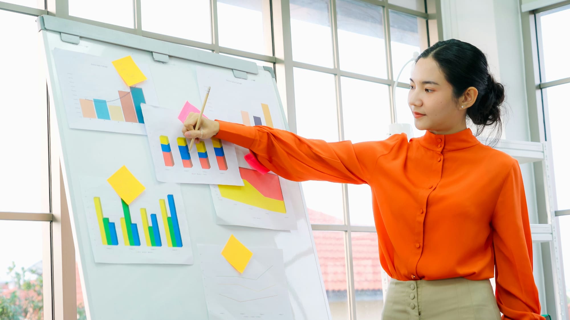 A woman standing next to whiteboard using a pen to point at some bar charts.