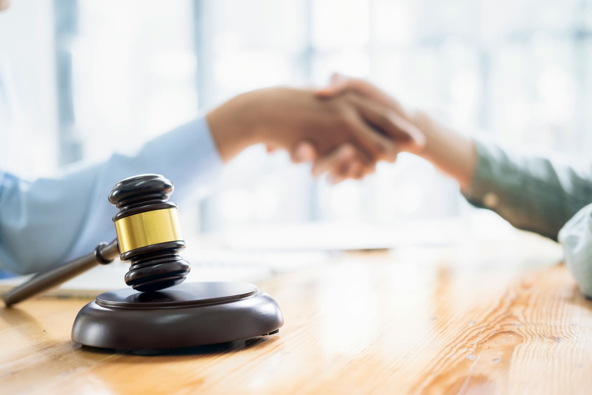 Two people shaking hands in the background with a gavel in the foreground.