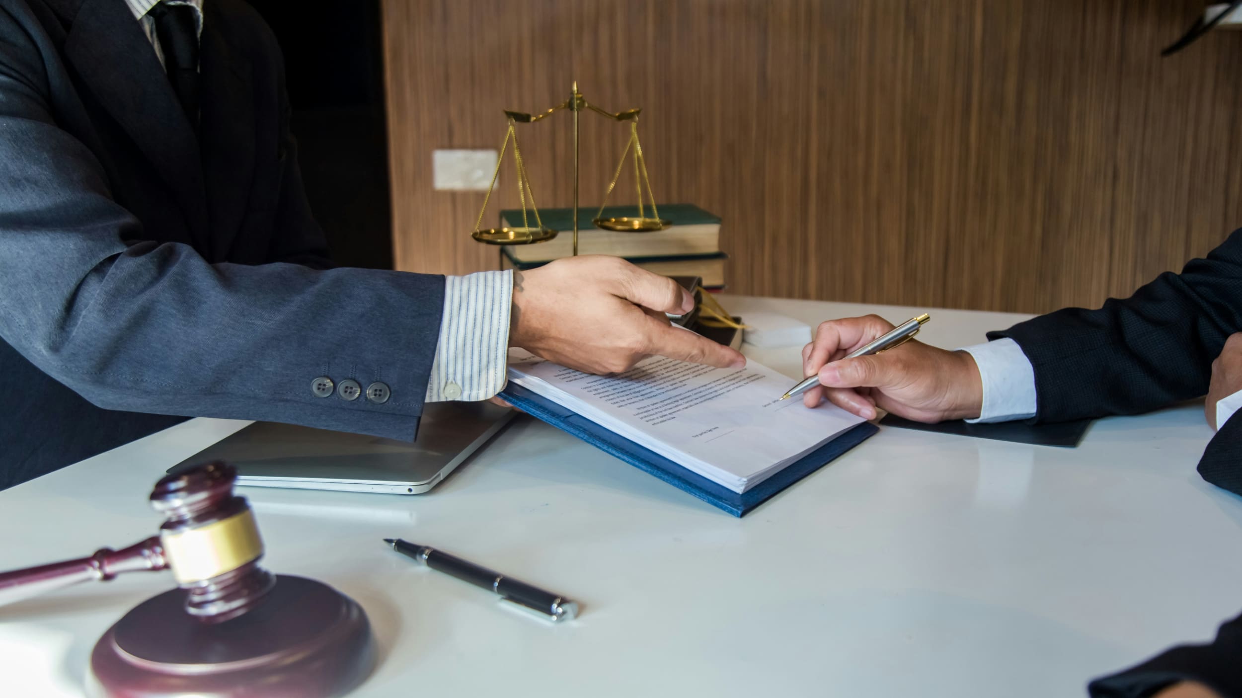 Two business people pointing at notepad on desk with gavel next to it.