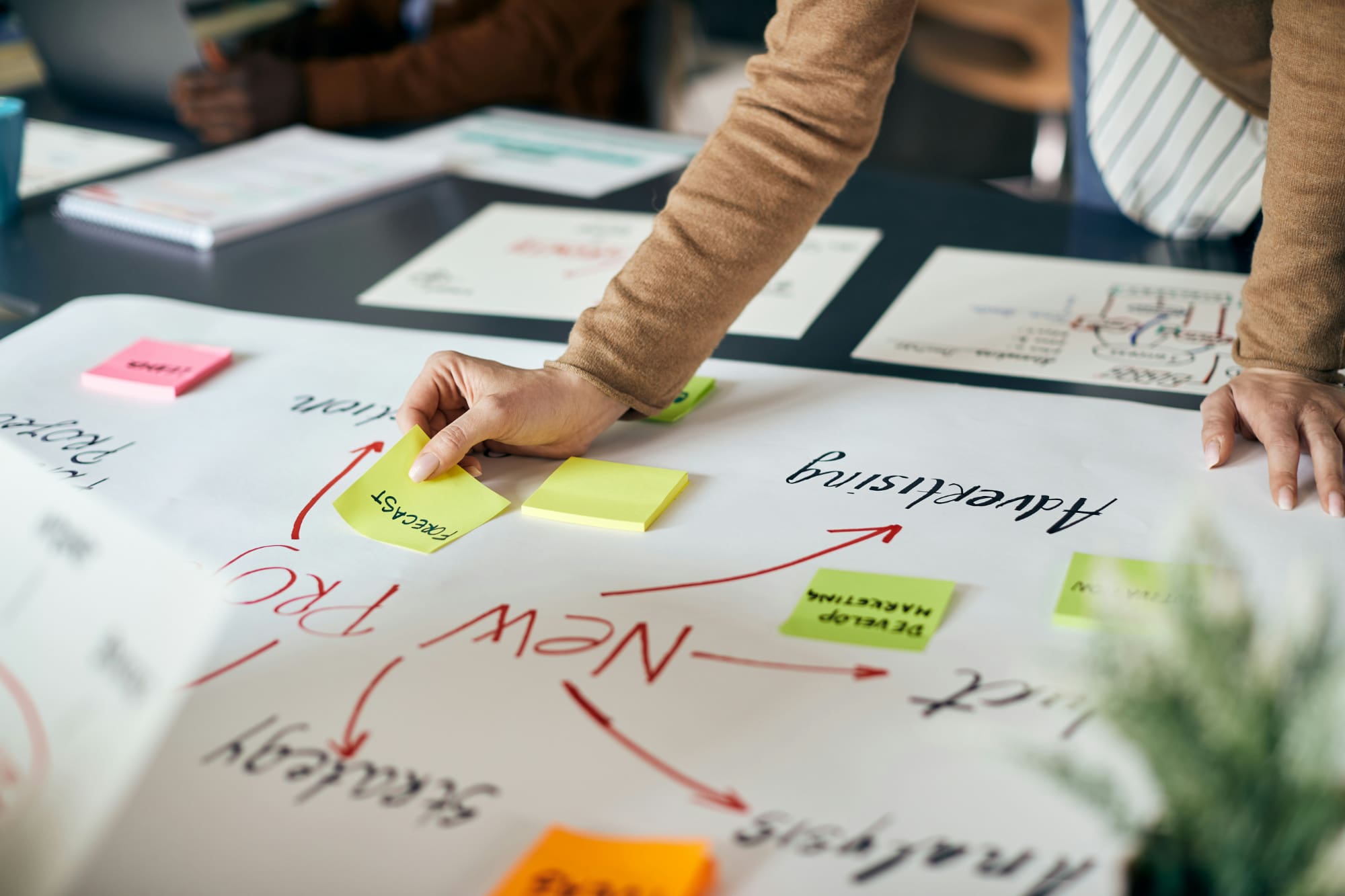 A business person adding a yellow sticky note to a project plan.