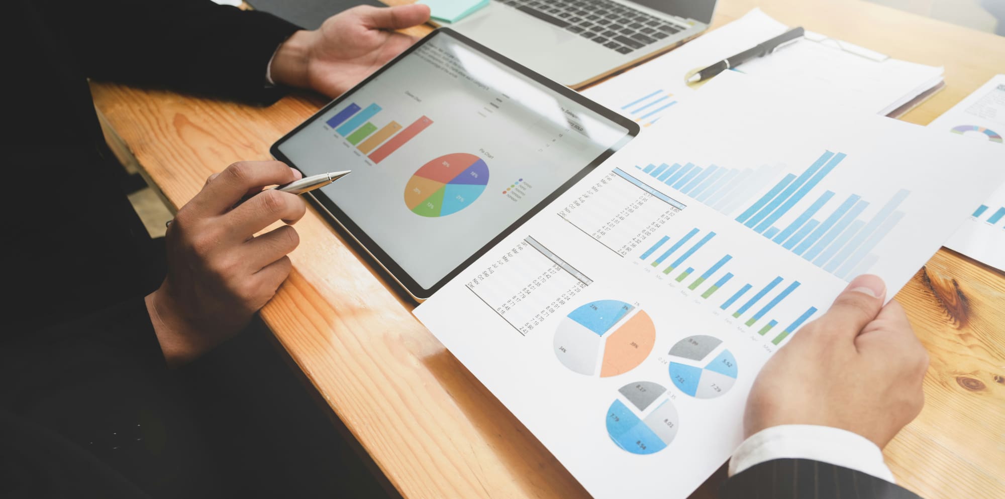 Business people pointing at various charts printed out on paper and on a tablet.