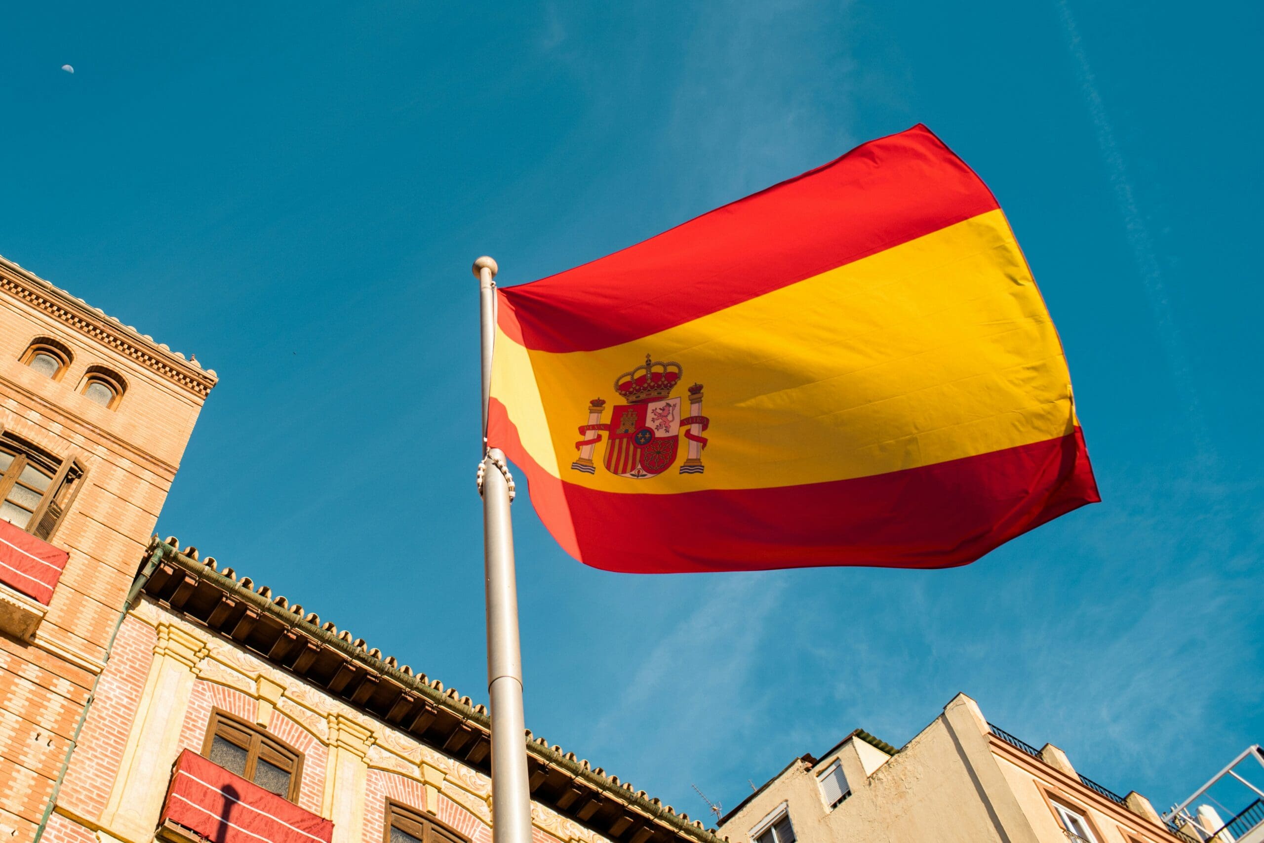 A spanish flag flying in front of spanish buildings.