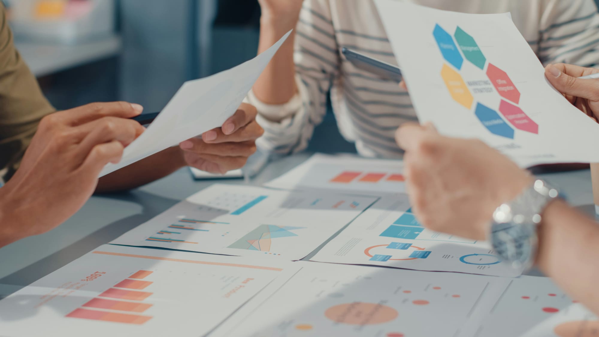 Three people sat at desk looking through several printed business graphs.