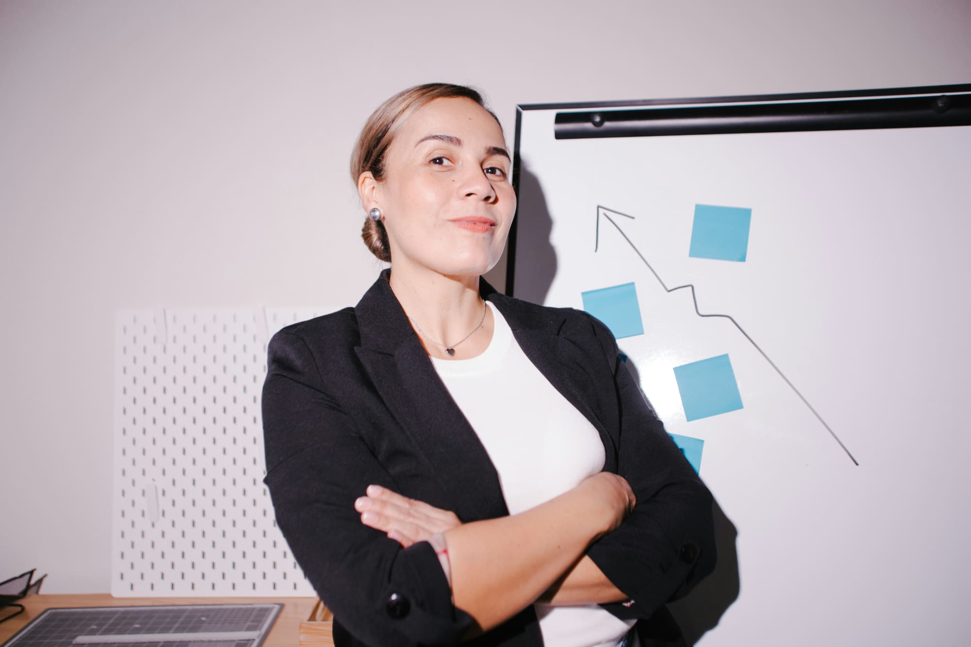 Woman standing with arms crossed in front of whiteboard with blue post-it notes strategically placed on it.