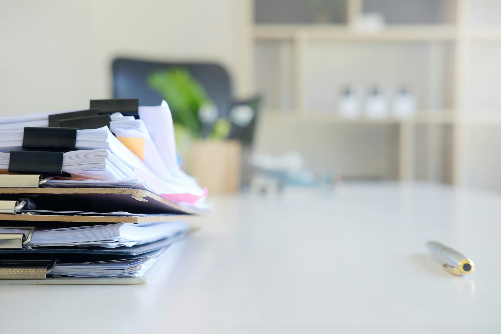 Big stack of EcoVadis documents in folders on desk next to pen with shelves in background