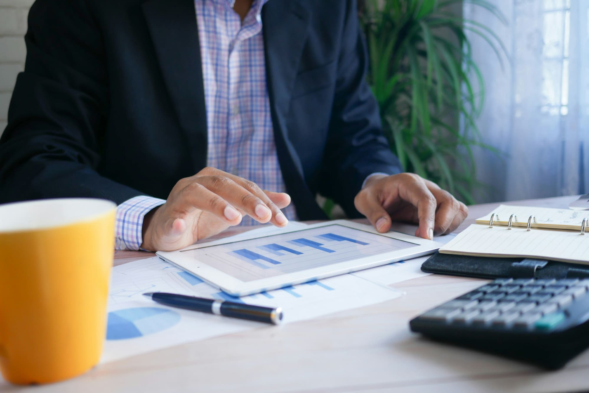 Man in suit sitting behind desk swiping through business charts on a digital tablet