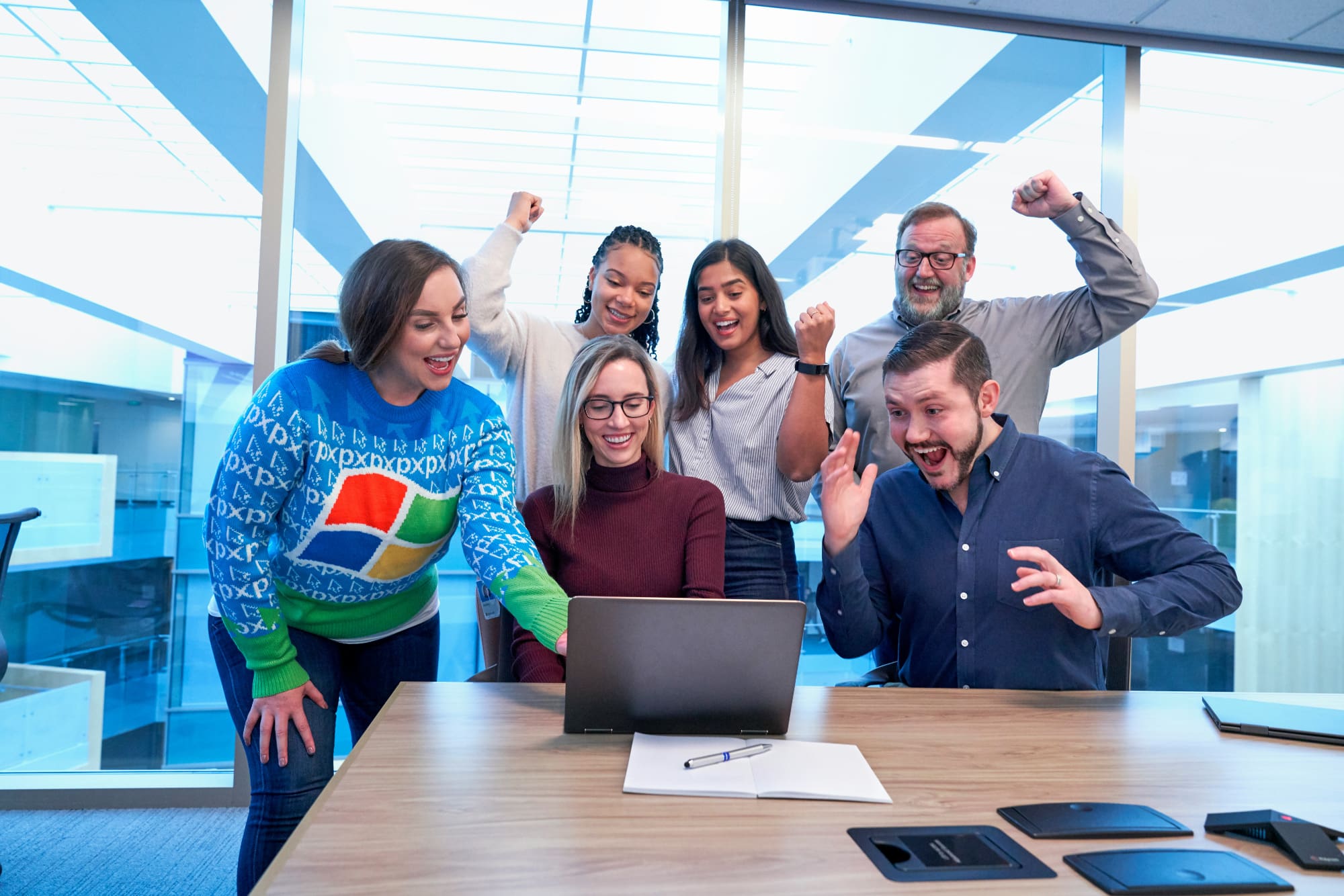 Several office workers in an office standing behind desk with laptop on it celebrating.