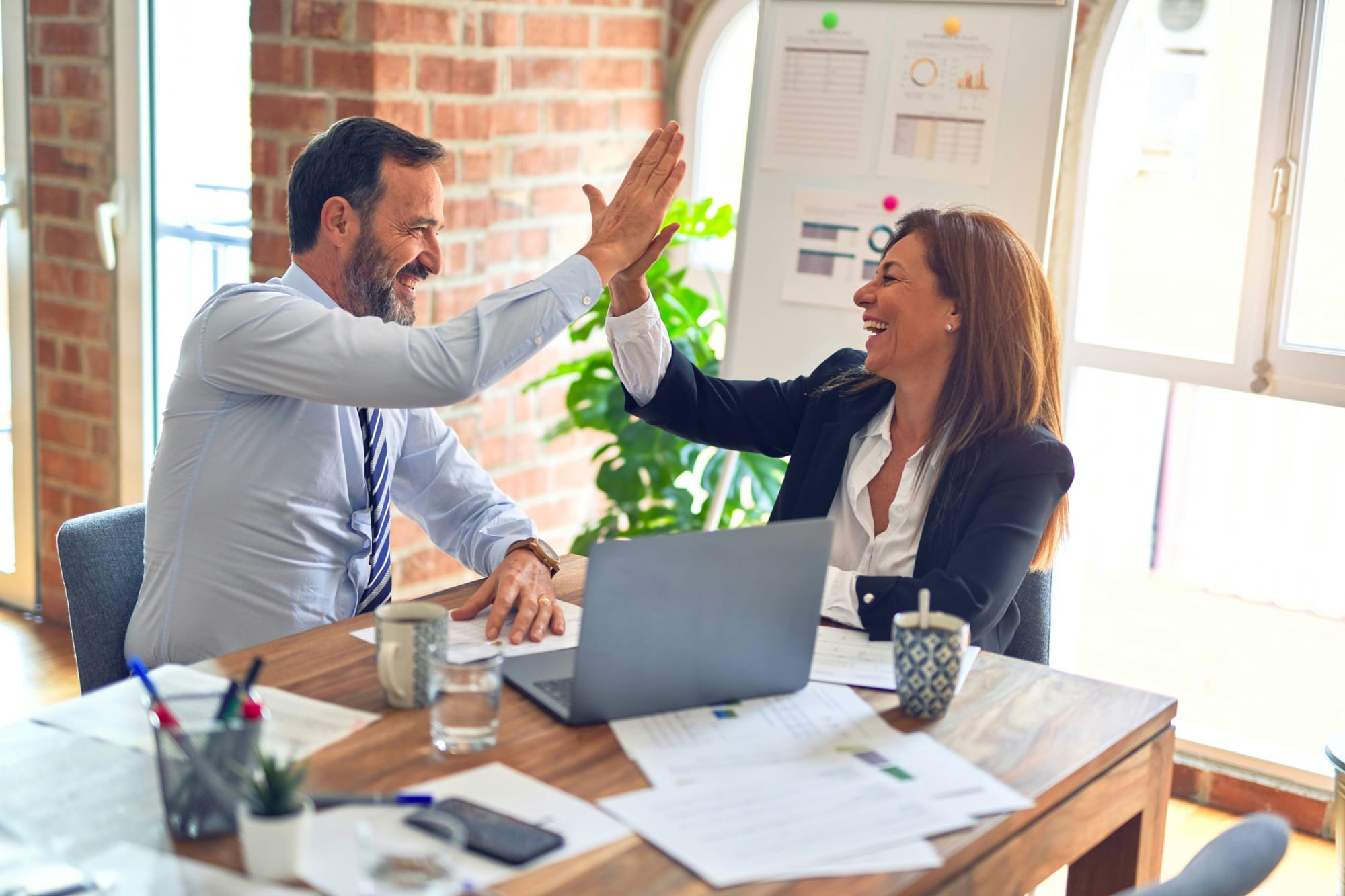 Two business people high-fiving behind desk.