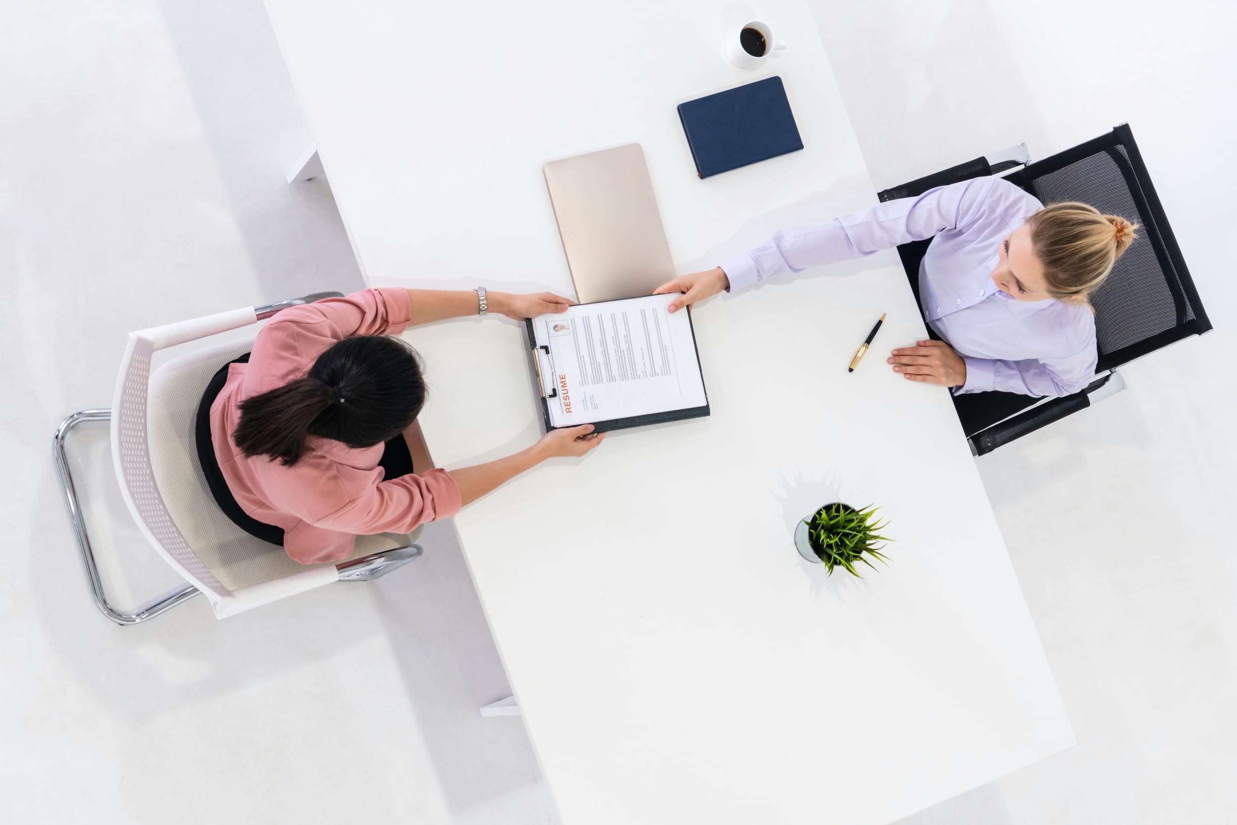 Overhead shot of an interview process, with a candidate handing their CV to the interviewer across a desk.