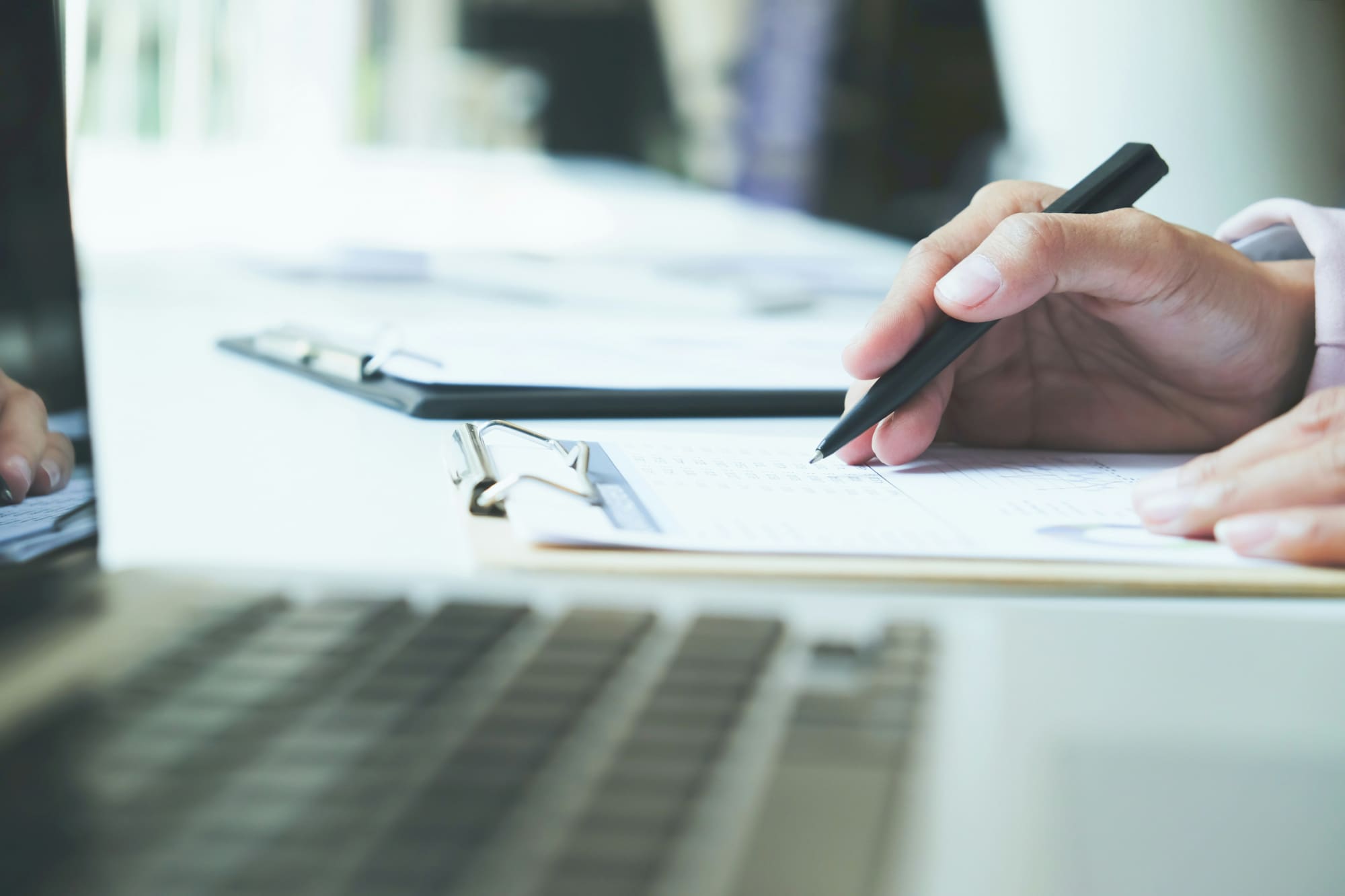 Hand holding pen to search through EcoVadis questionnaire on desk next to laptop